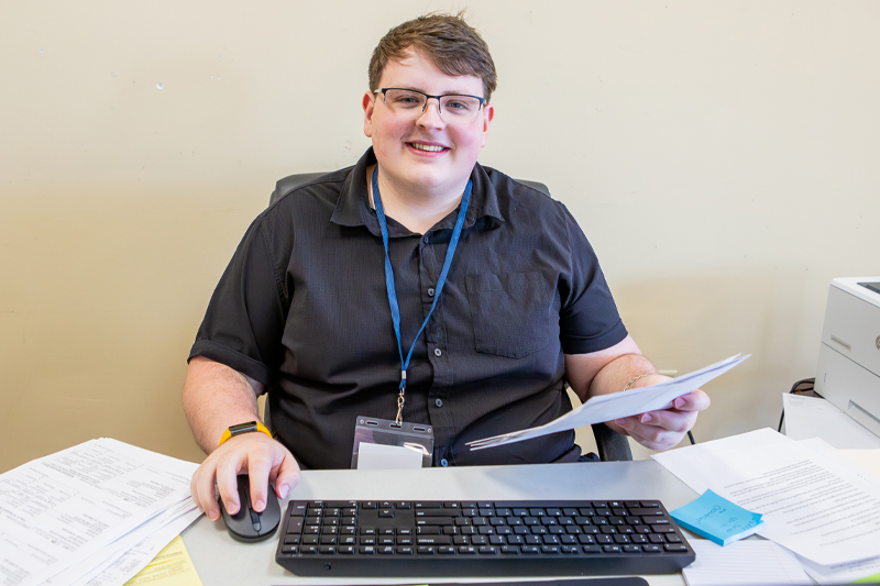 Student smiling in front of computer with paperwork