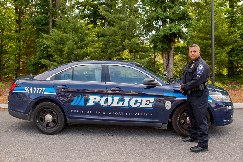 Officer Delgado stands beside his CNU Police car.