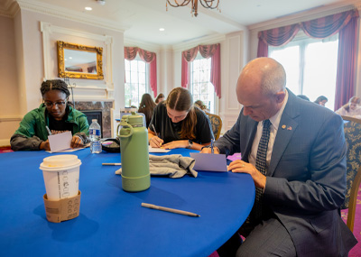 President Kelly in the foreground writes a thank you note to first responders with other students at a table.