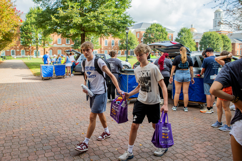 A freshman walks with a younger family member to move into a residence hall