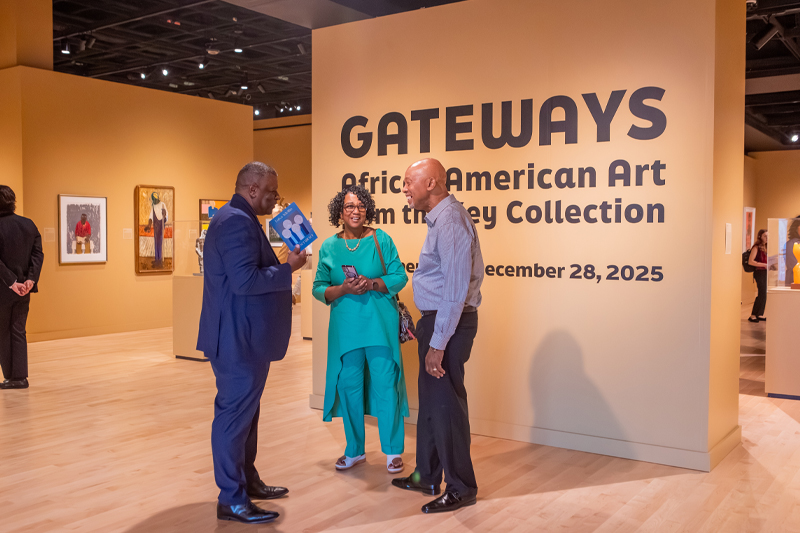 Three individuals stand at the entrance to the Gateways exhibition in the Torggler Fine Arts Center at Christopher Newport University
