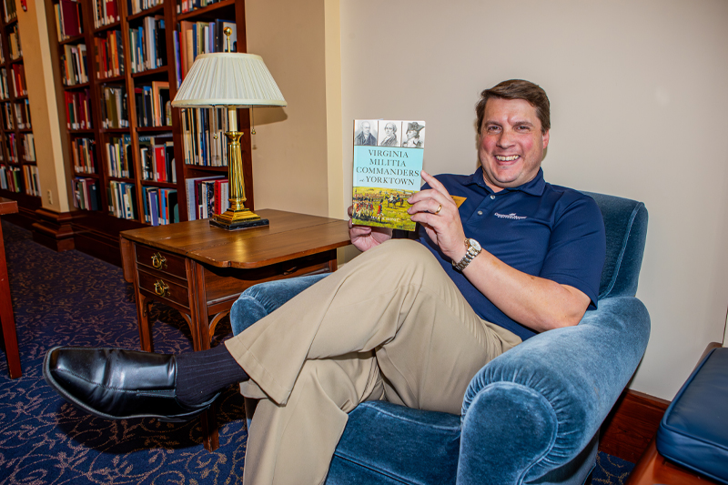 Sean Heuvel sits in a chair holding up his new book.