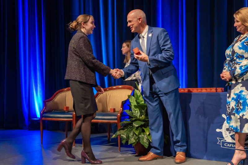CNU President Bill Kelly hands a student a class ring on stage. 