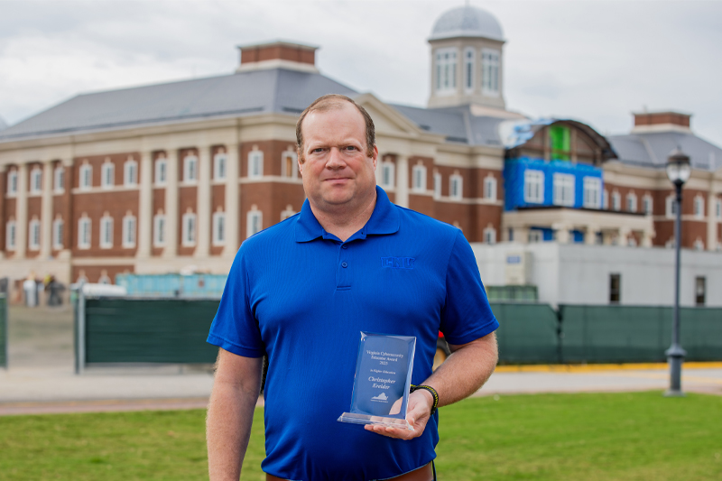 Dr. Christopher Kreider wears a CNU blue polo while holding his glass Virginia Cybersecurity Educator Award