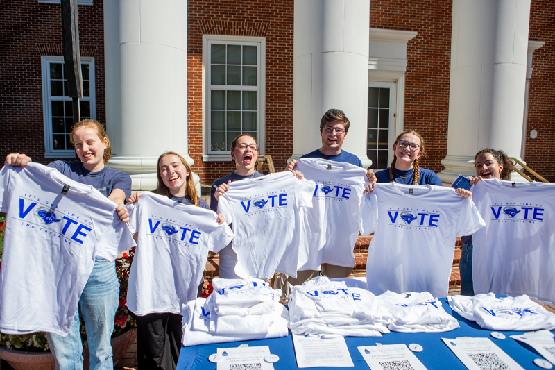 Students smiling and holding up t-shirts