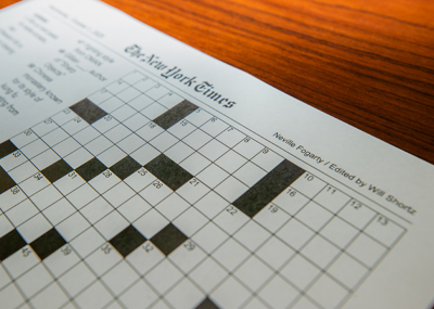A close-up of a printed The New York Times crossword puzzle, created by Neville Fogarty, lying on a wooden table.