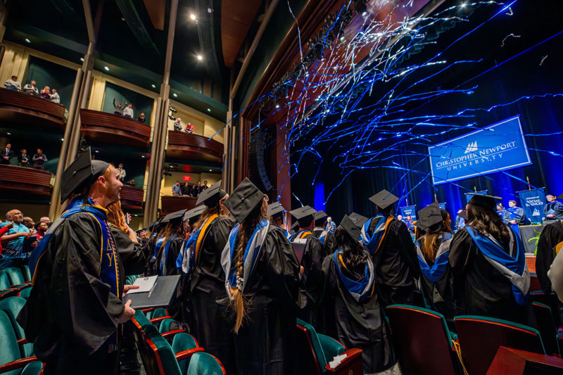 A wide shot of a graduation ceremony from the perspective of students in the audience. 