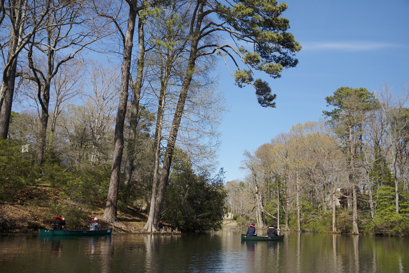 Two boats floating down the river with trees in the horizon