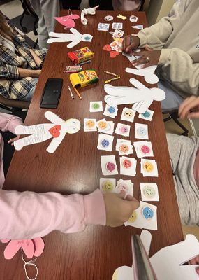 Crayons and stickers being used on paper dolls