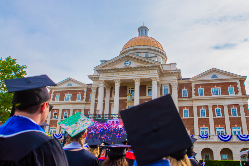 The backs of graduate caps looking up to Christopher Newport Hall.