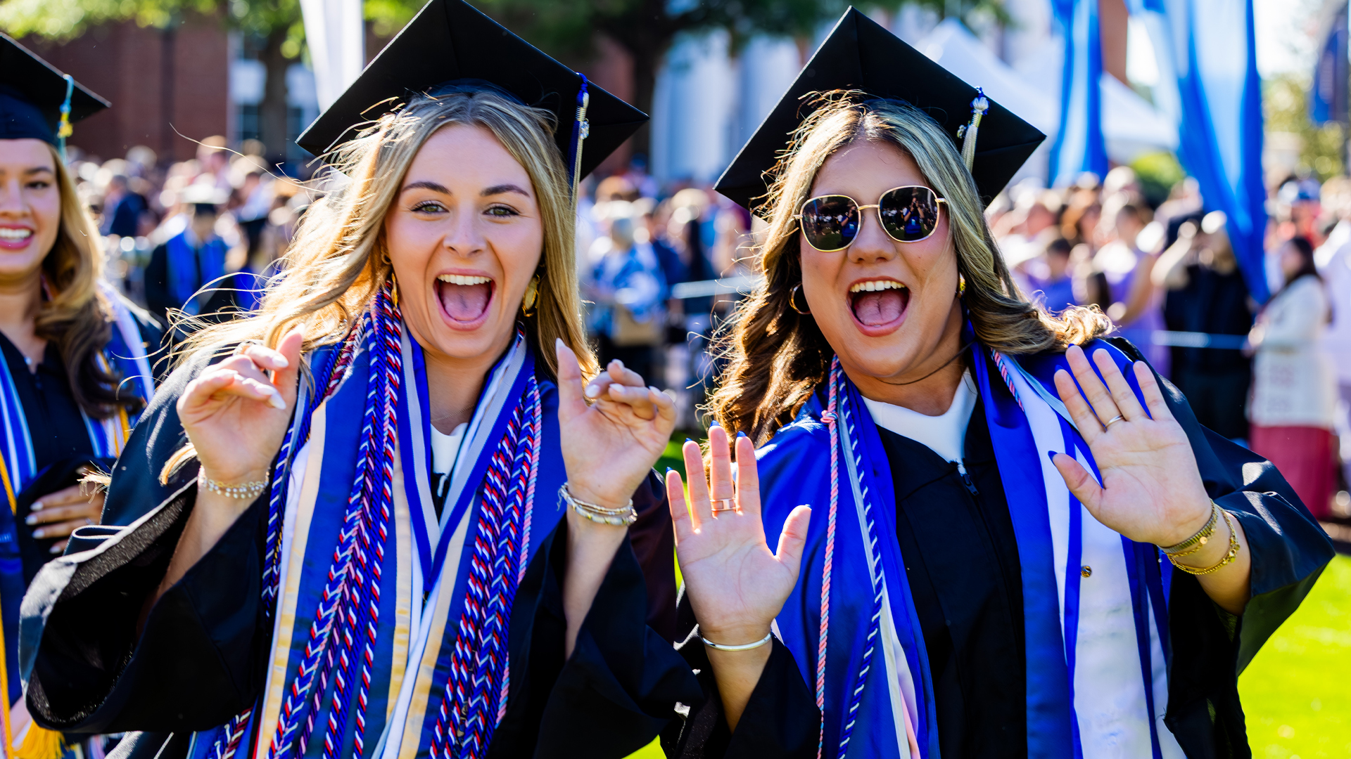 Two women in graduation regalia smile big for the camera