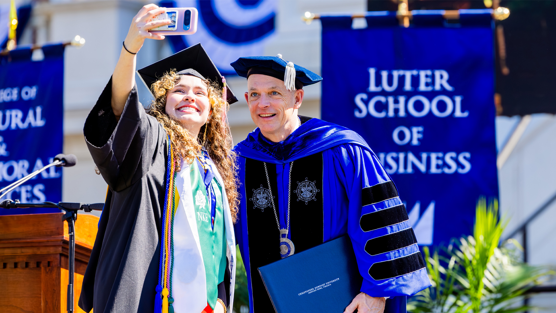 A student holds her phone out to take a selfie with CNU President Bill Kelly after receiving her diploma.