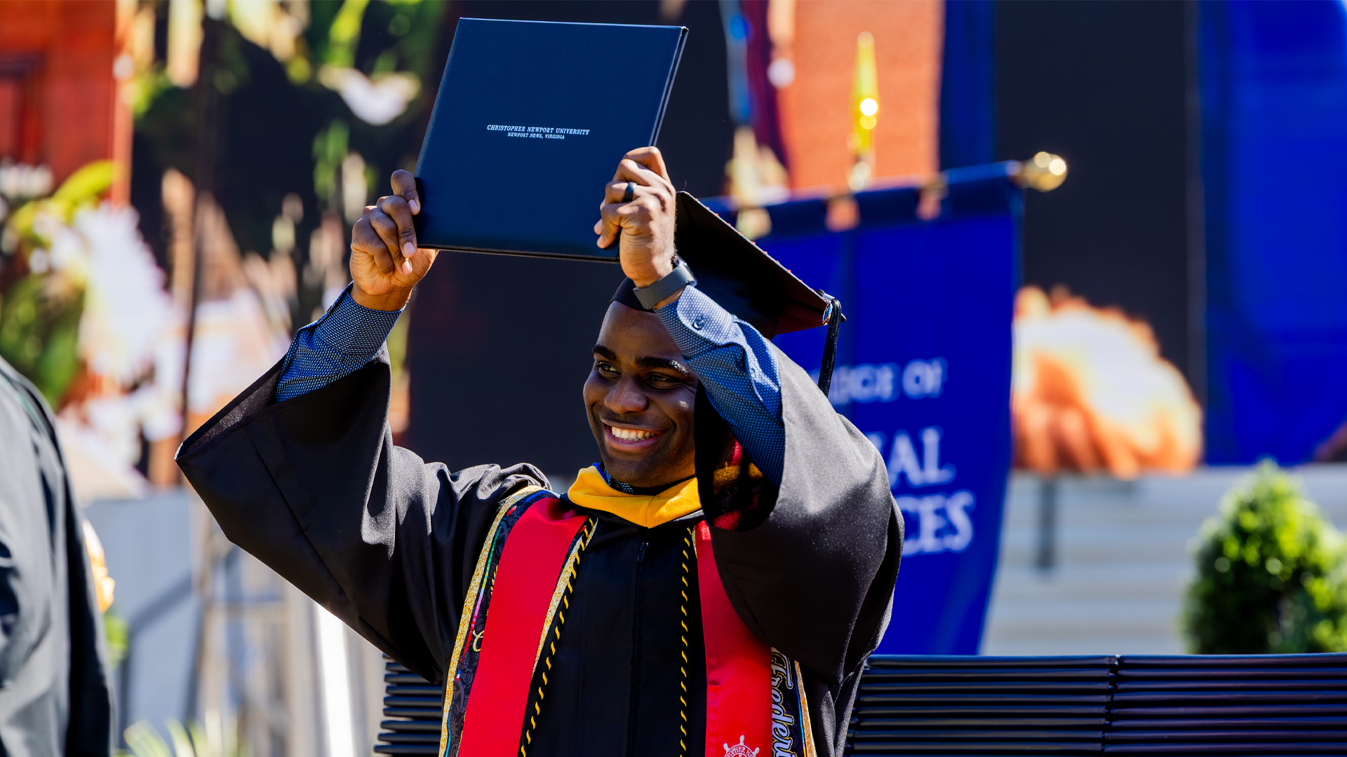 A student raises his diploma over his head while crossing the stage.