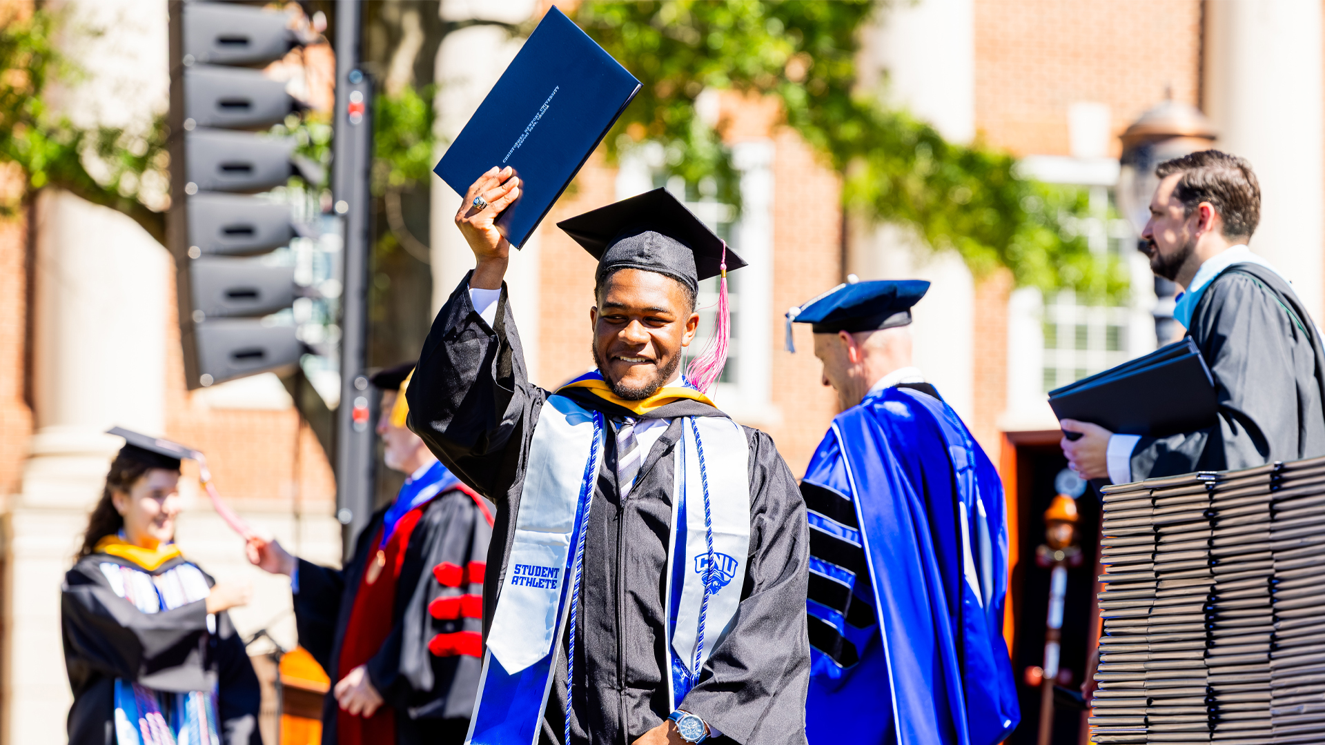 A student in graduation regalia holds their diploma up crossing the stage.