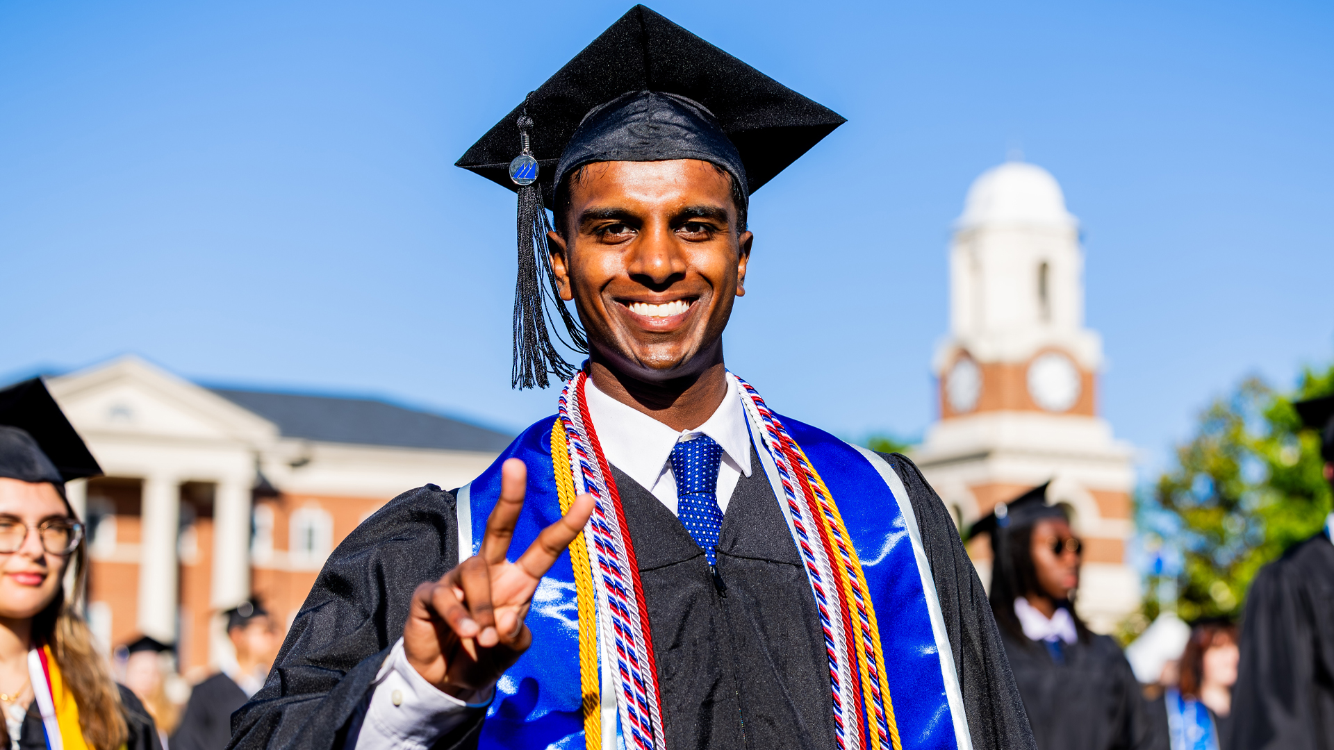 A male in graduation regalia gives a peace sign.