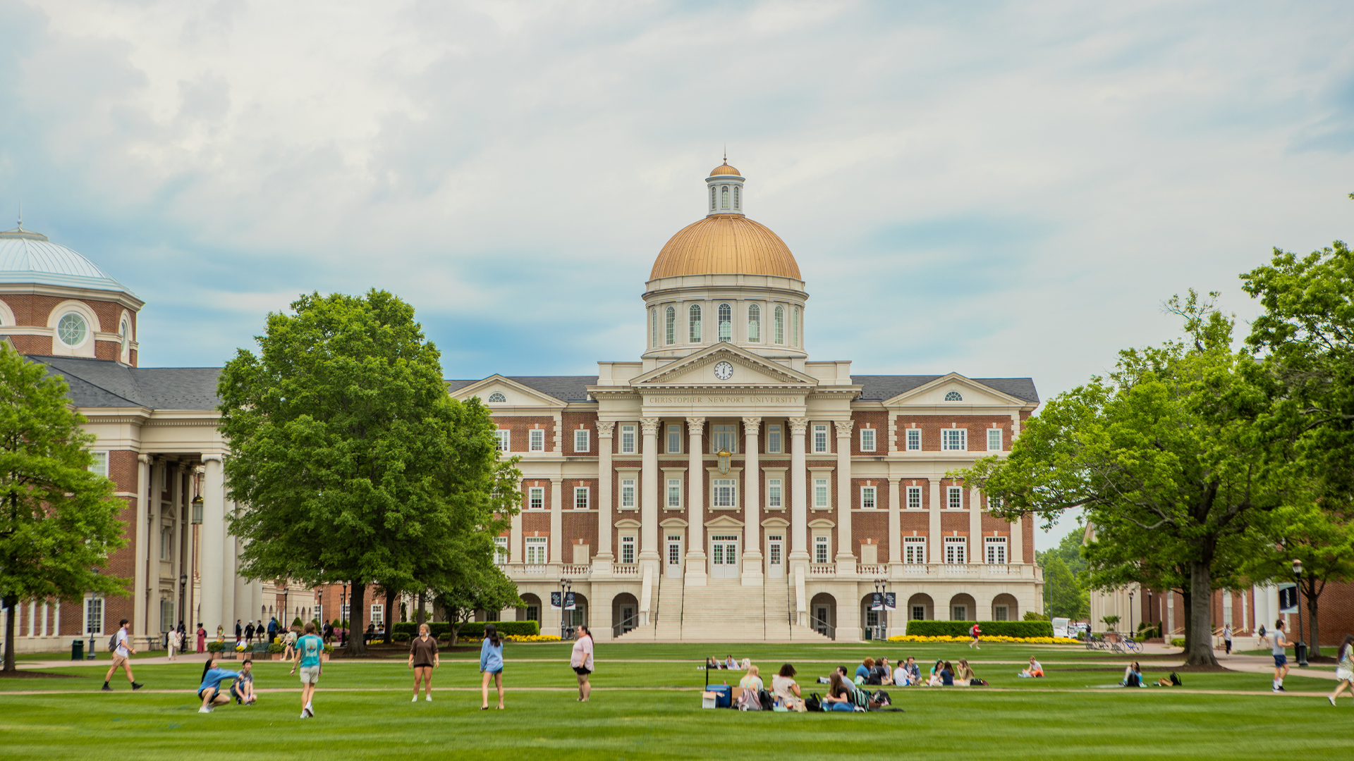 A view of CNU's Great Lawn with students sitting and enjoying warm weather in front of Christopher Newport Hall