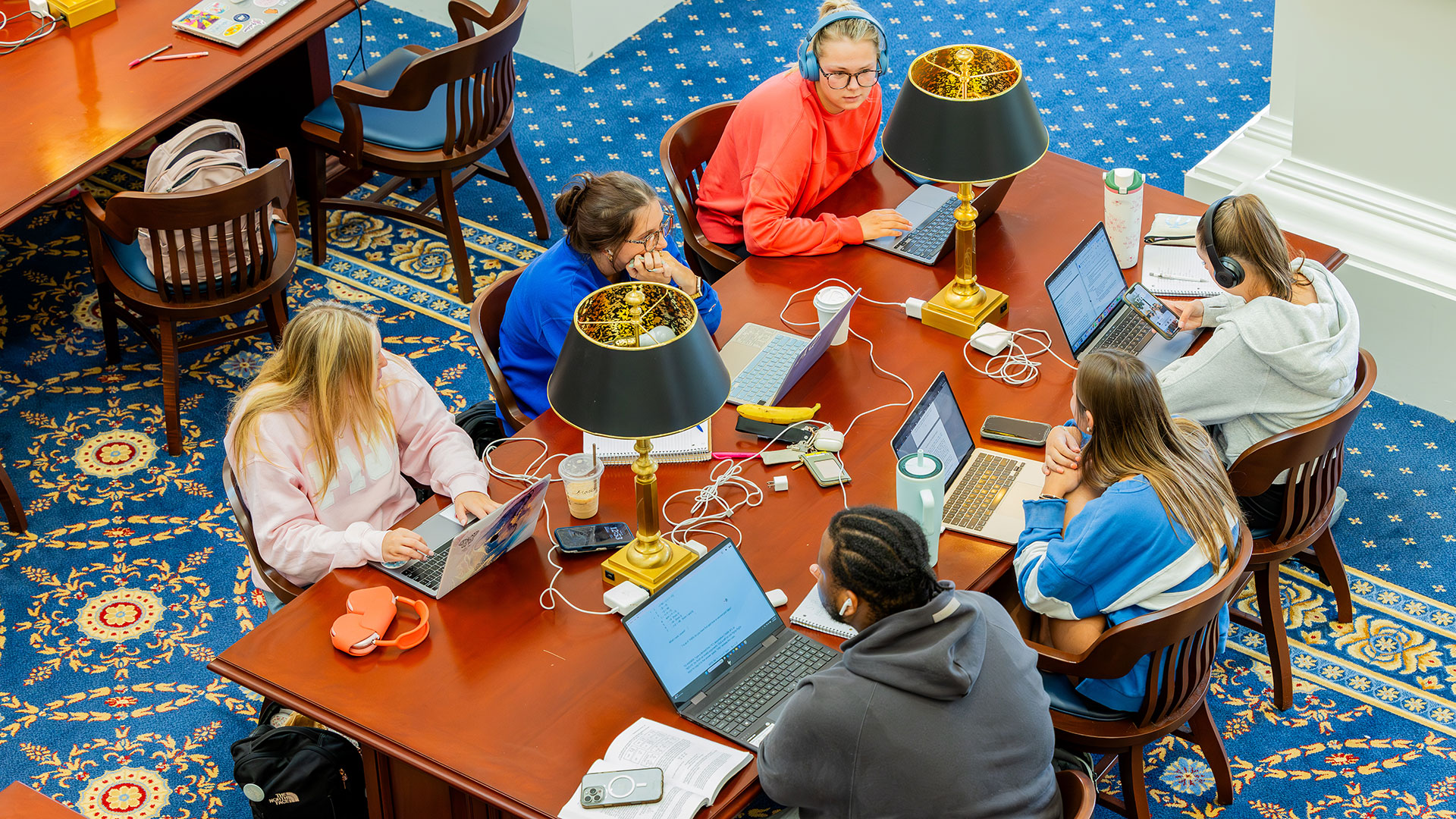 A group of students sit at a table in the library with laptops open studying for finals