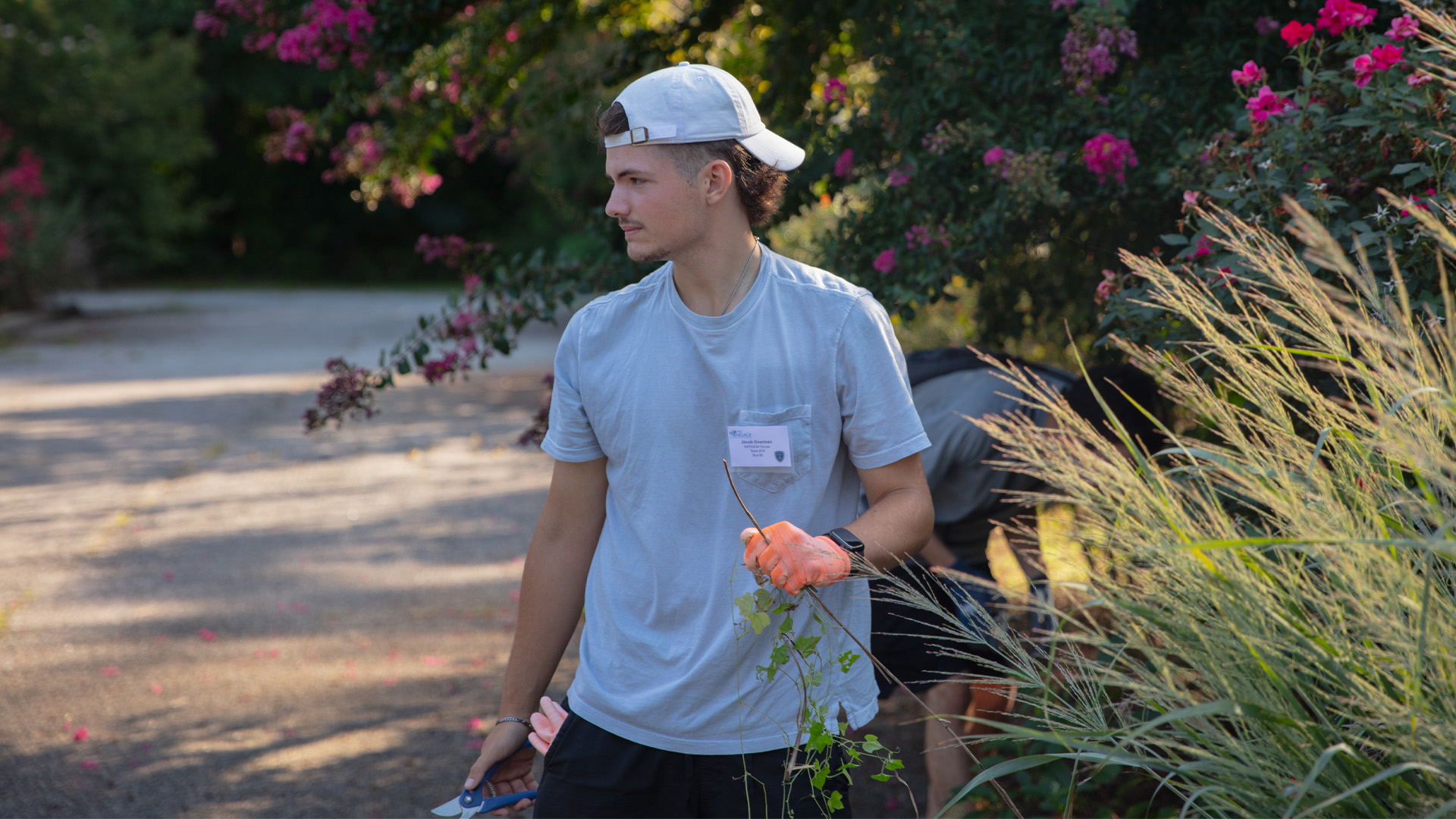 A student wearing a backwards hat cuts shrubs