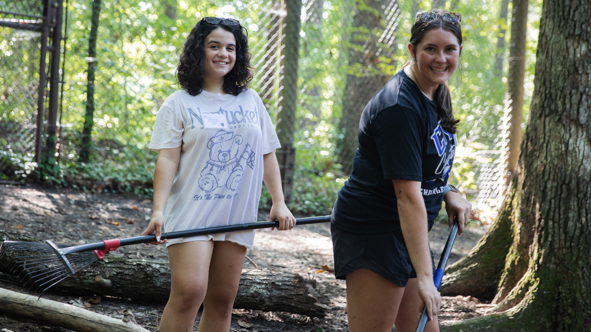 Two students hold rakes inside an animal enclosure