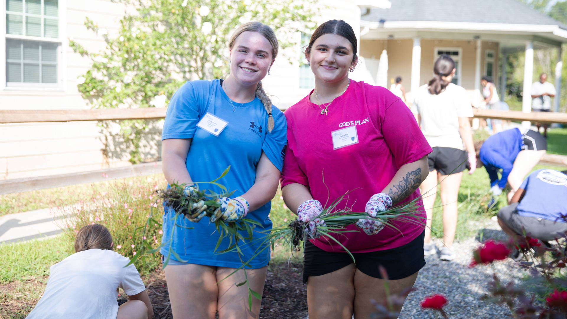 Two students smile while holding weeds they've pulled