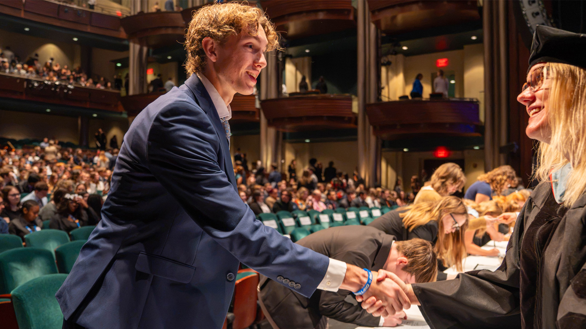 A student in business attire shakes the hand of a faculty member after receiving their penny
