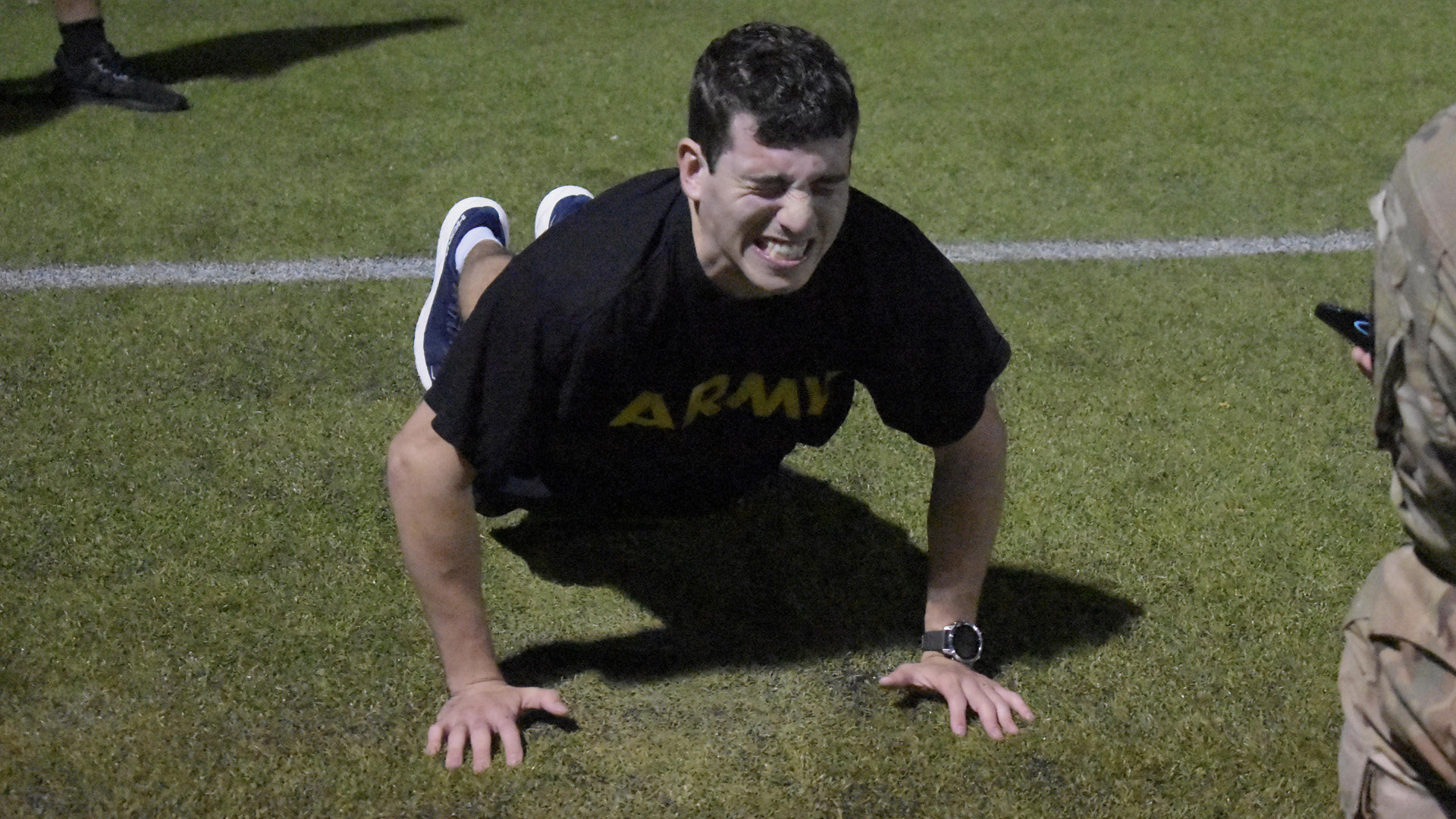 A student wearing a black Army t-shirt grimaces while performing a push-up