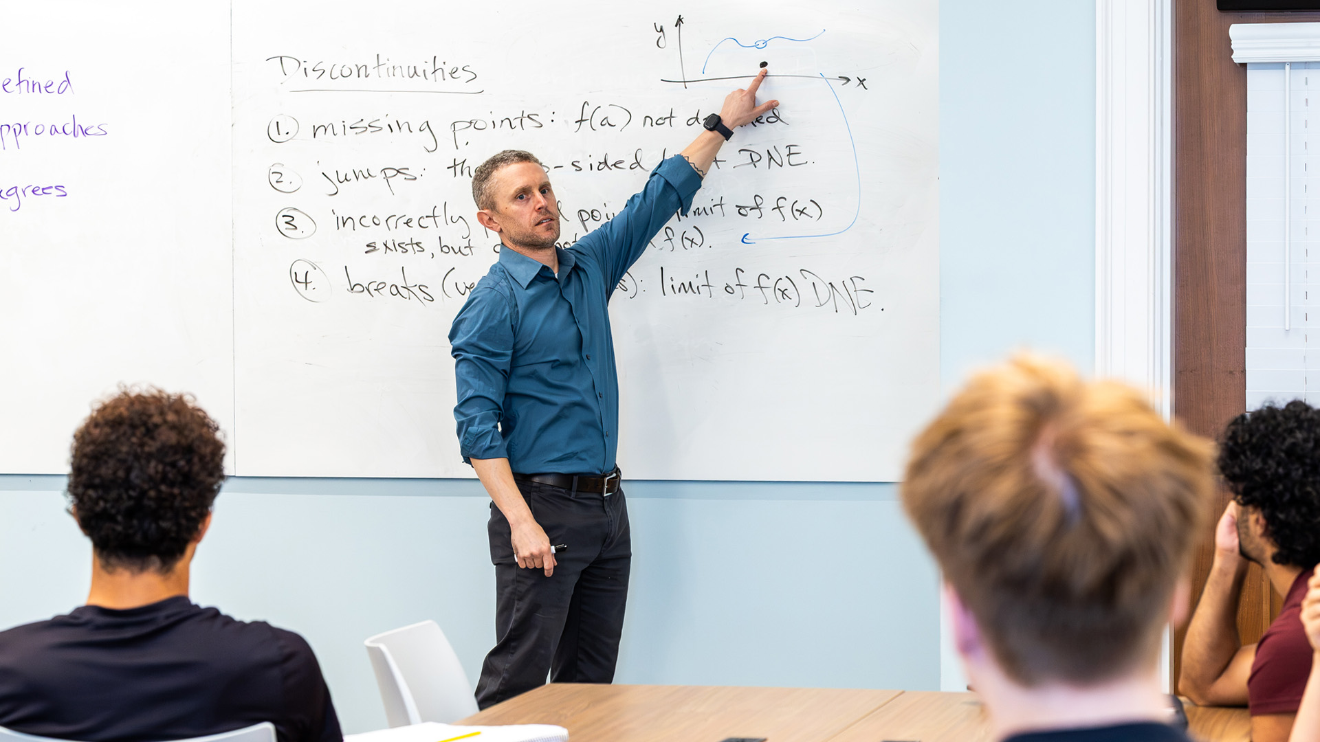 Matt Morena stands in front of a whiteboard looking out to a class of students.