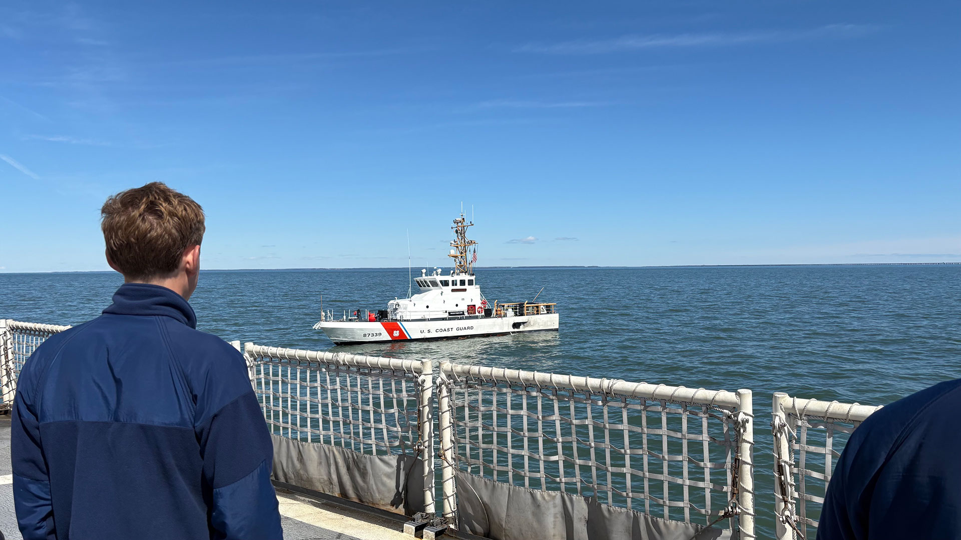 The back of a student looking out at the sea where a US Coast Guard ship sits.