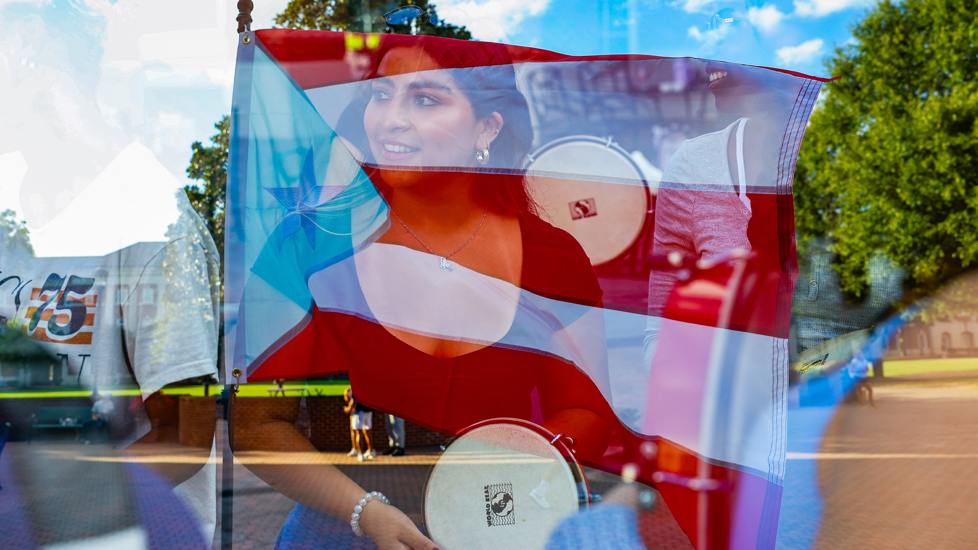 A Puerto Rican flag is transposed over a student holding a pandereta
