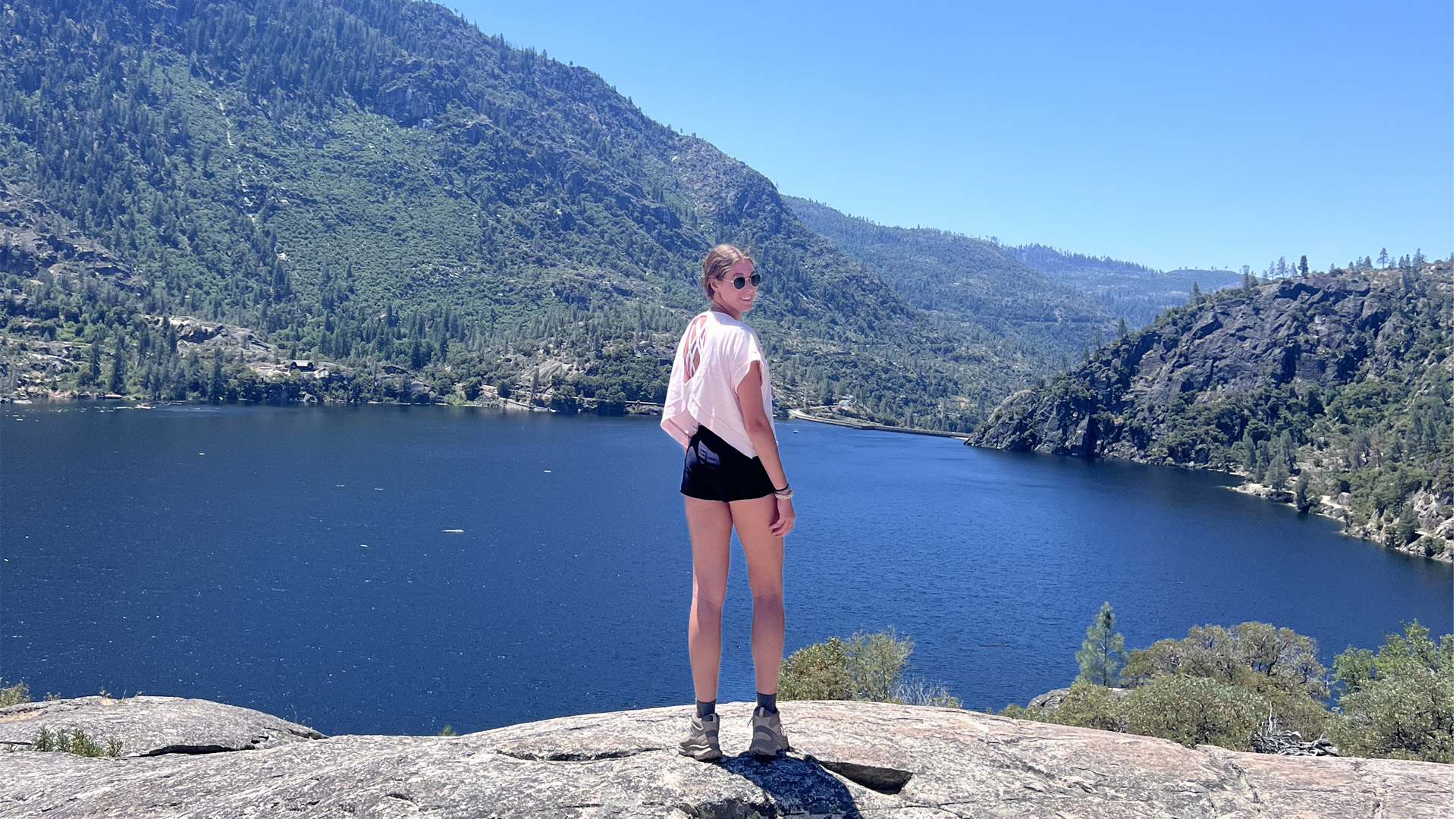A student looks over her shoulder in front of a lake and mountains