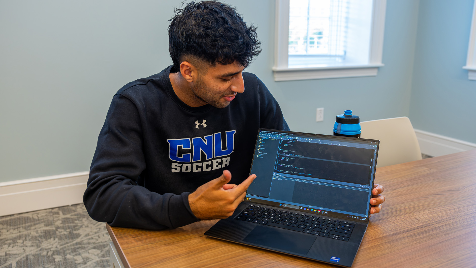 A student wearing a CNU soccer sweatshirt points to a laptop screen.