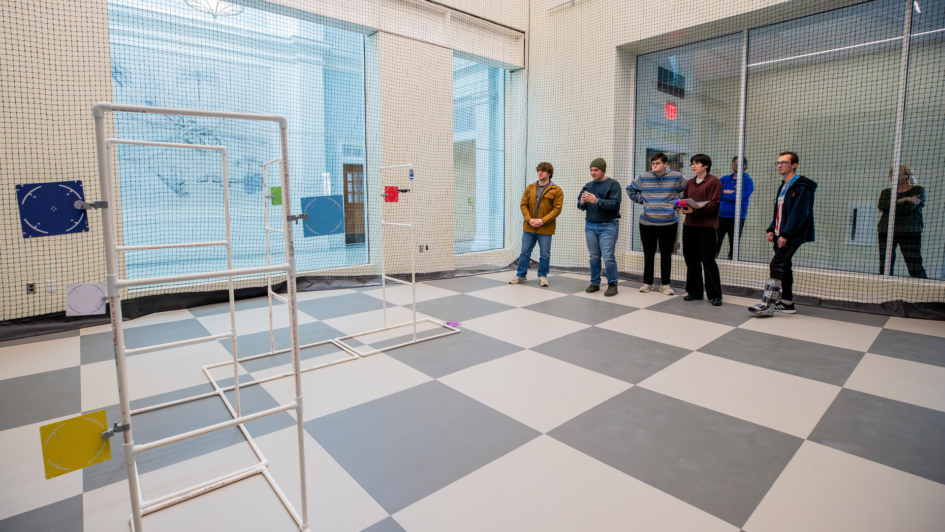 Students stand at one of a drone testing room that has netting and pvc pipe obstacles for drones