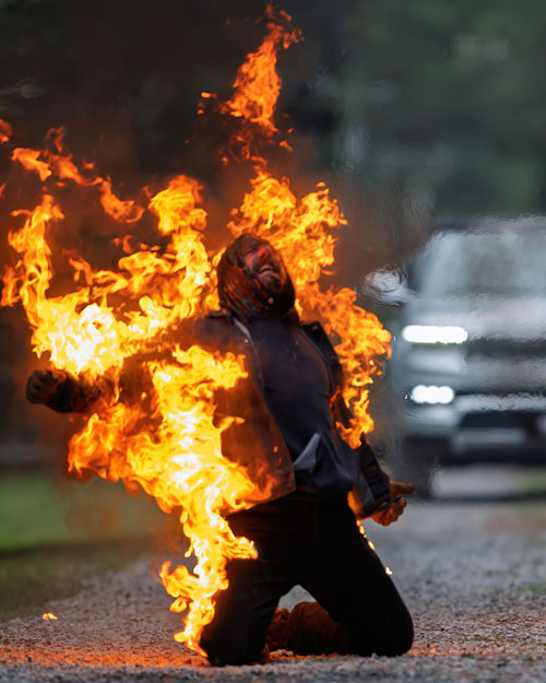 Greg Poljacik is on fire while wearing a burn suit. Flames and dark smoke are coming off of the suit