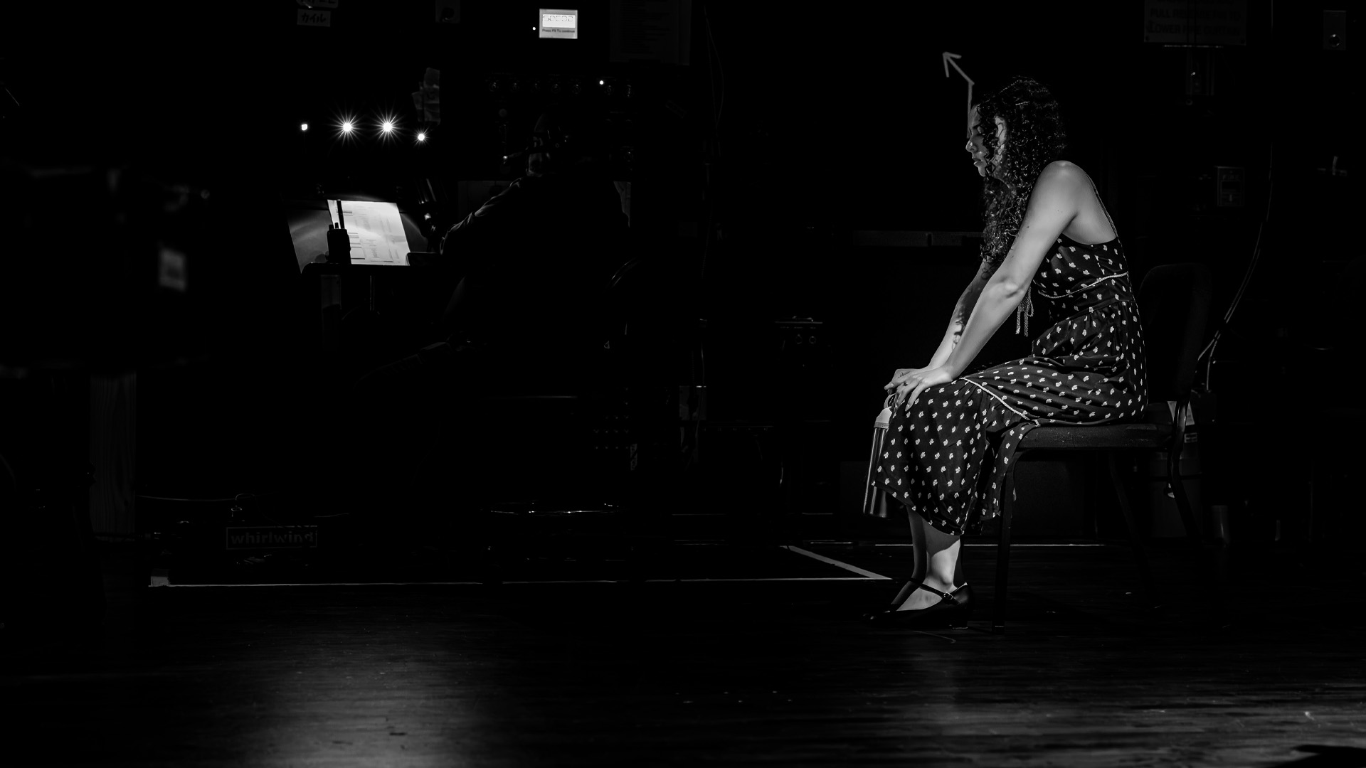 Black and white image of Erin Rigby sitting on the stairs backstage in a dress