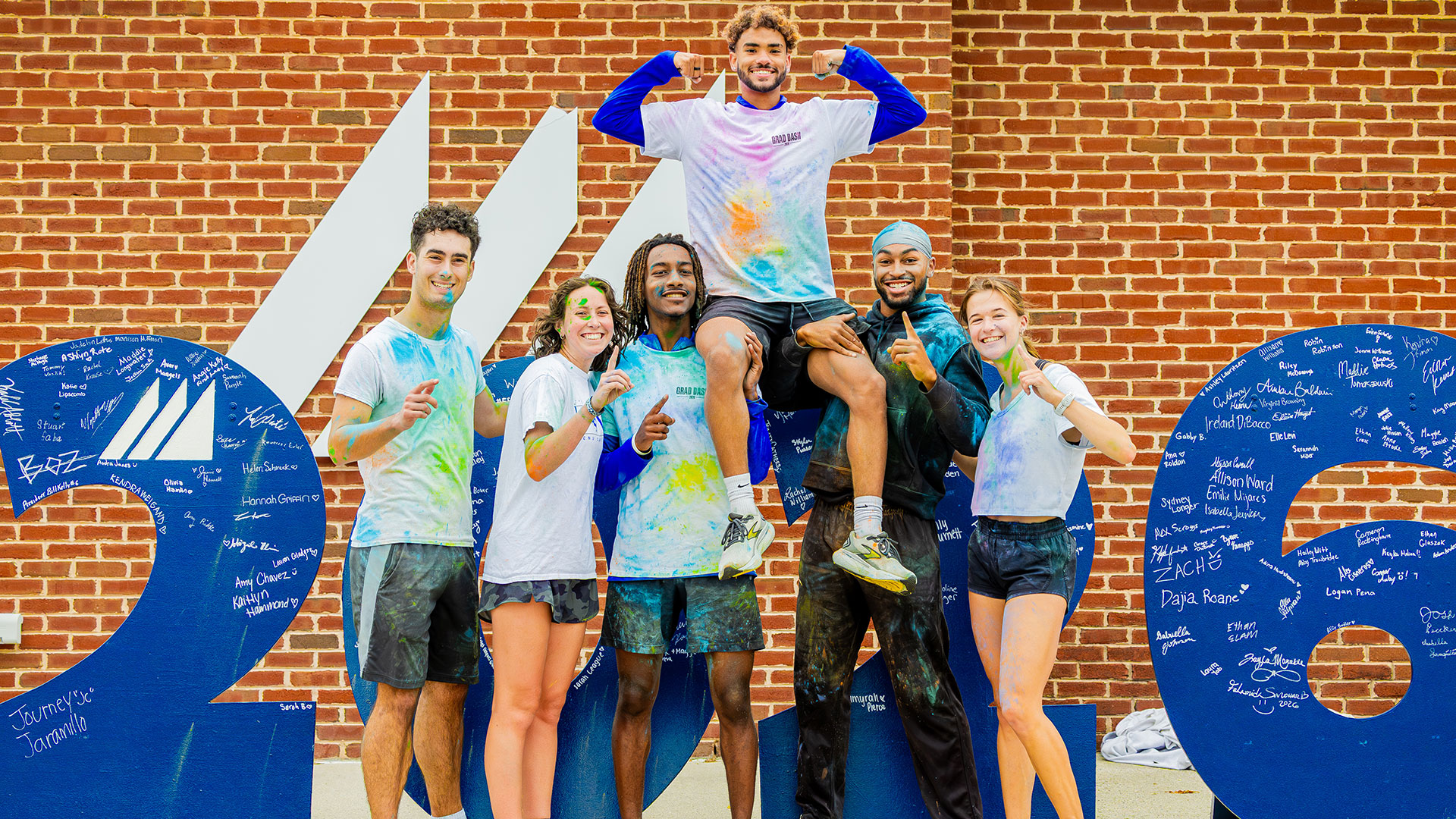 Students dyed from a color run stand together in front of wooden numbers