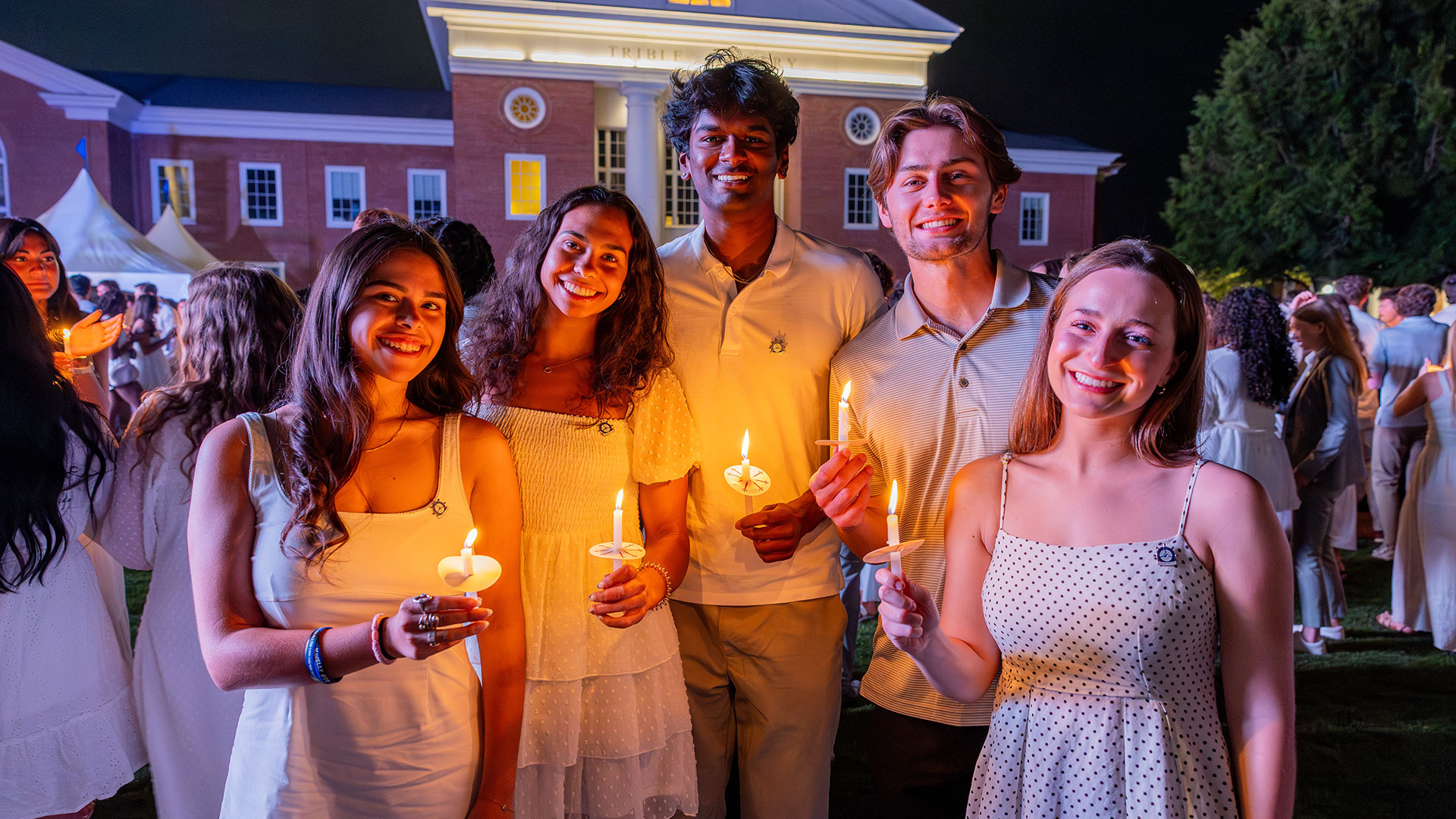 Students wearing white hold lit candles
