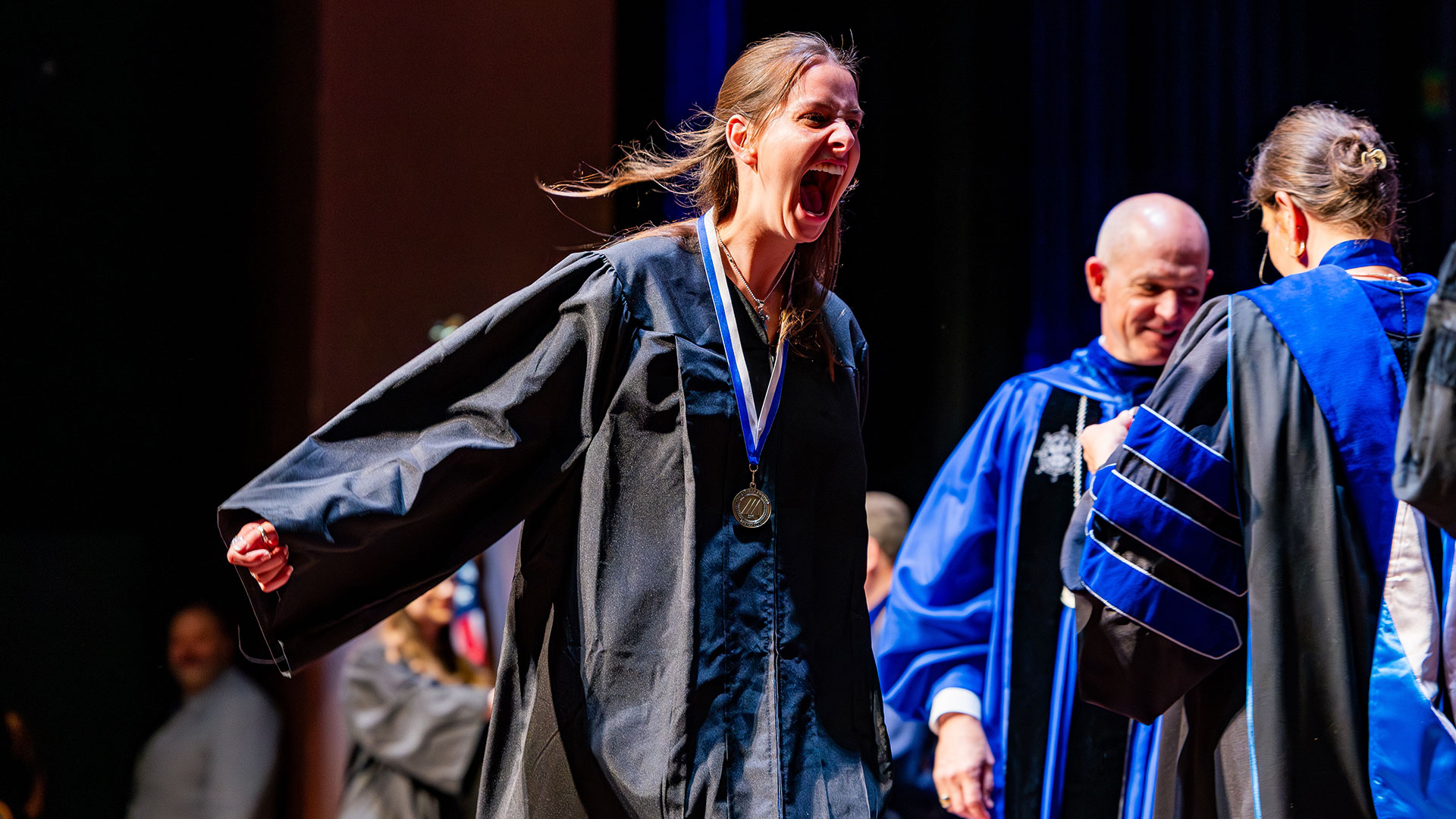 A graduate wearing a medal cheers enthusiastically