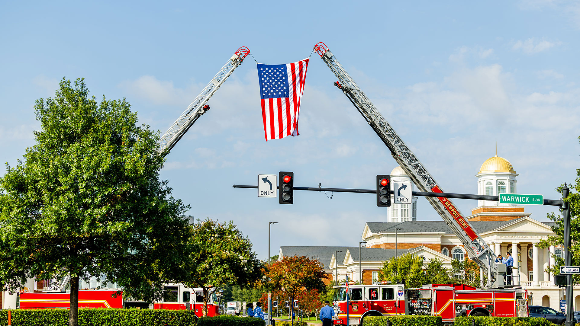 a flag hangs from two extended fire engine ladders in front of CNU's campus