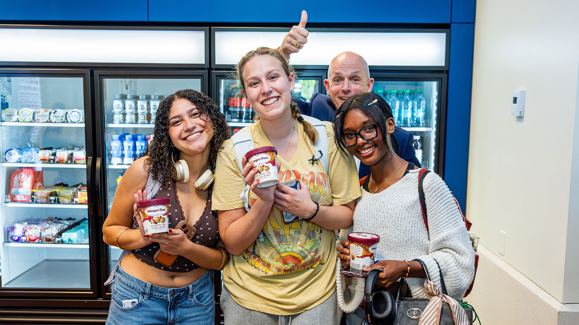Three students hold quarts of ice cream while CNU President Bill Kelly smiles and gives a thumbs up behind them