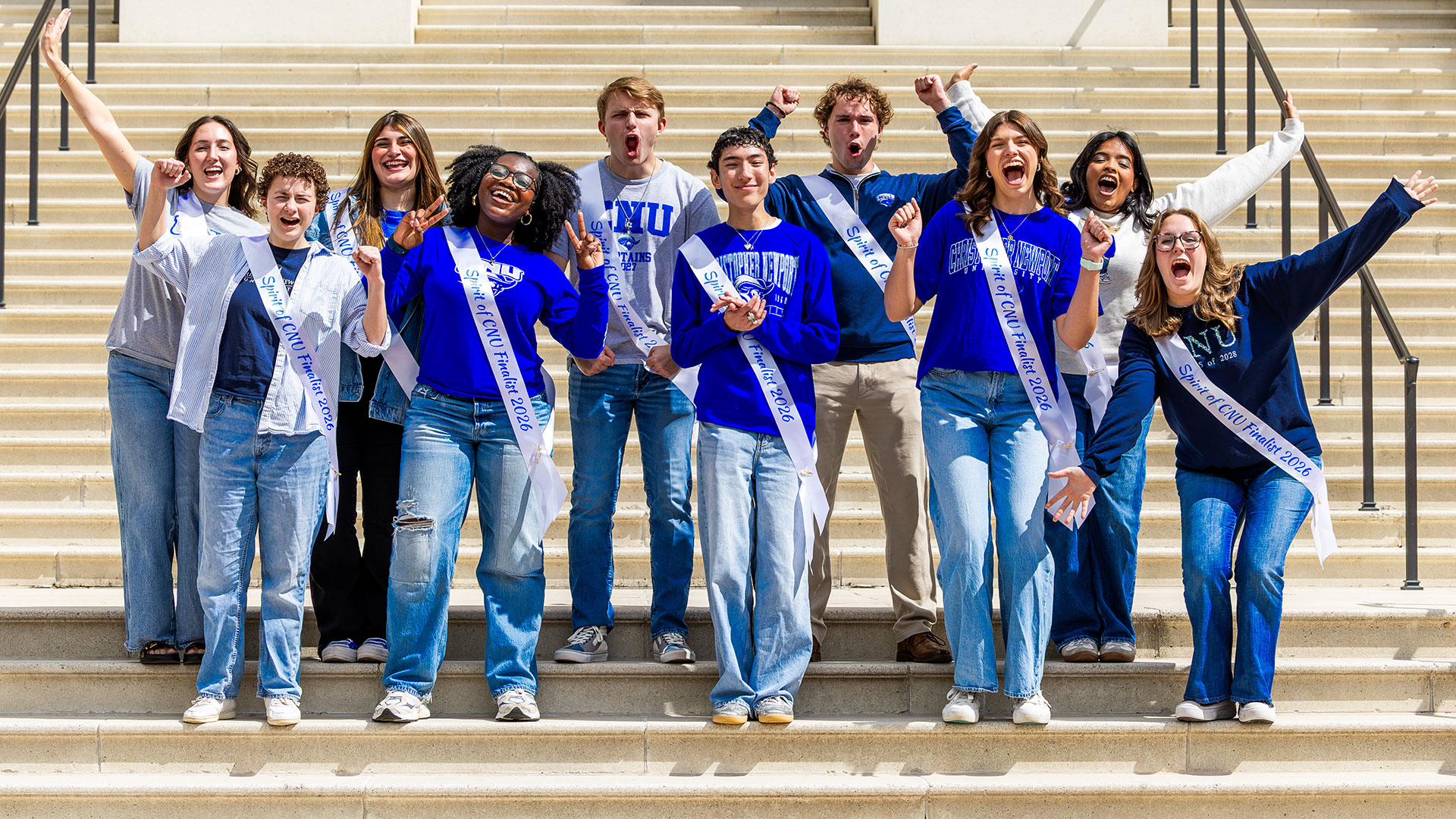 A group of cheerful college students wearing sashes that read Spirit of CNU Finalist 2026 posing and raising their arms in celebration on outdoor stone steps.